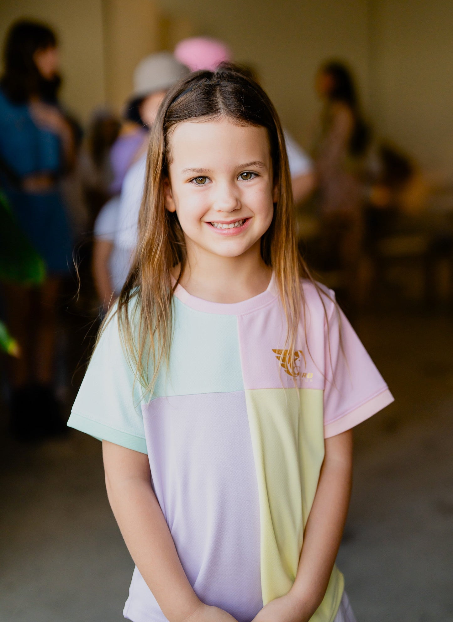 Girl wearing the colorful Betty Soccer Shirt with quad block pattern in pastel green, pink, yellow, and purple, featuring Hero Athletica gold leaf logo.