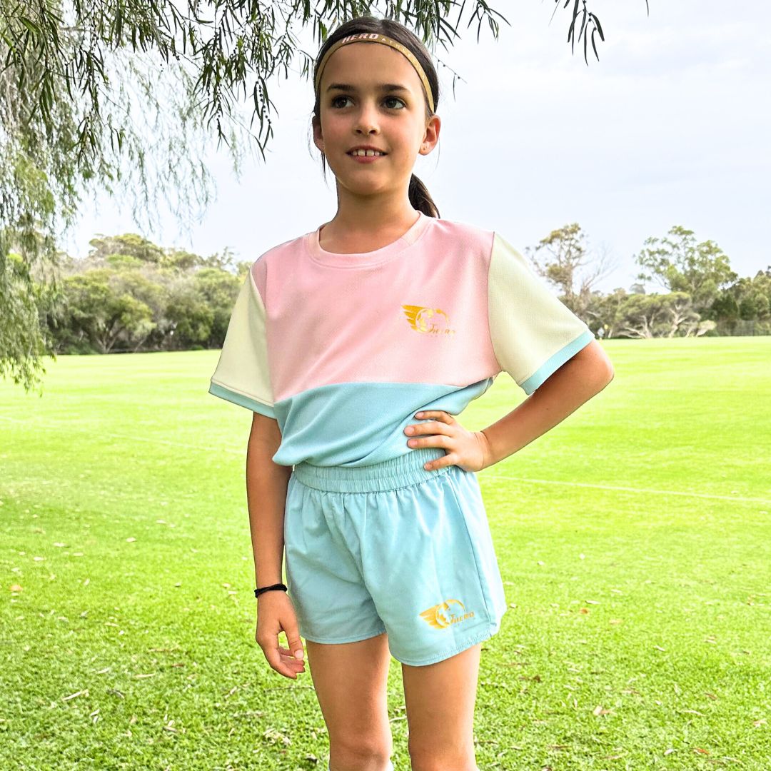 Pastel blue, pink, and cream Maggie Soccer Shirt with block design for girls, featuring a curved hem and Hero Athletica gold leaf logo.